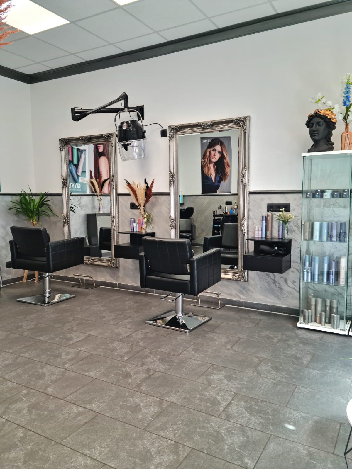 Ein leerer Friseursalon mit schwarzen Stühlen, großen Spiegeln und Pflanzen.